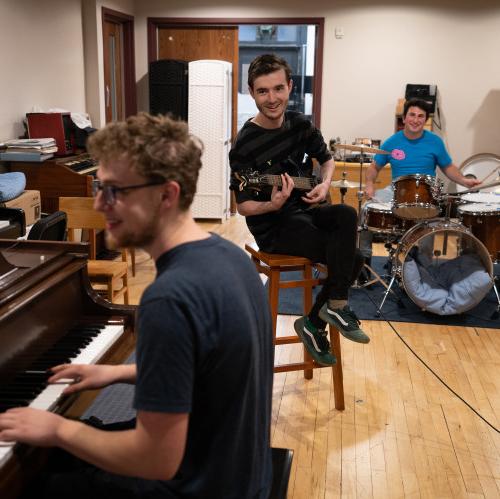 Three students play drums, guitar, piano in the Maple Tree Studio.